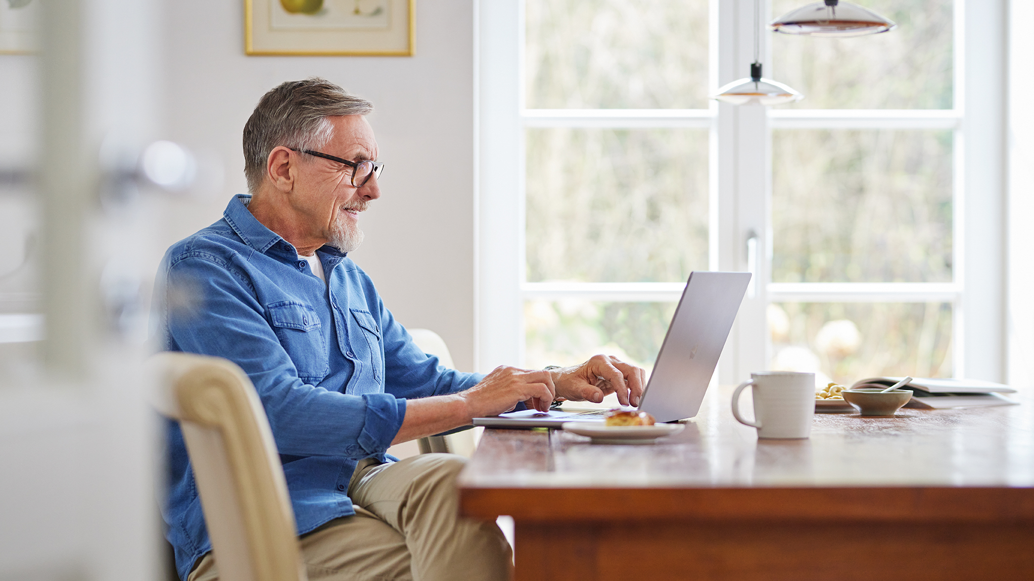 Mann sitzt am Esstisch und arbeitet am Laptop